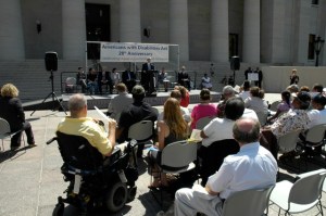 Photo of audience facing forward toward a stage, banner, and speaker.
