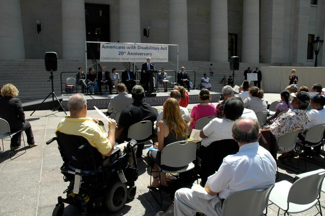 Photo of audience facing forward toward a stage, banner, and speaker.