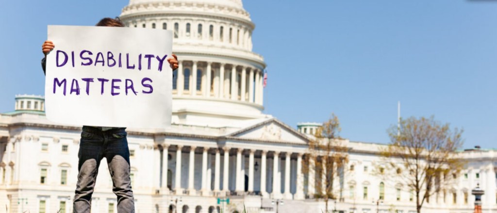 Picture of the United States Capitol with person holding a sign saying Disability Matters