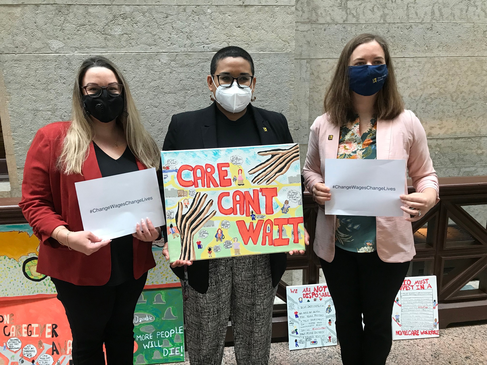 Three OOTF advocates hold signs supporting direct care workers and using the hashtag:  Change Wages Change Lives