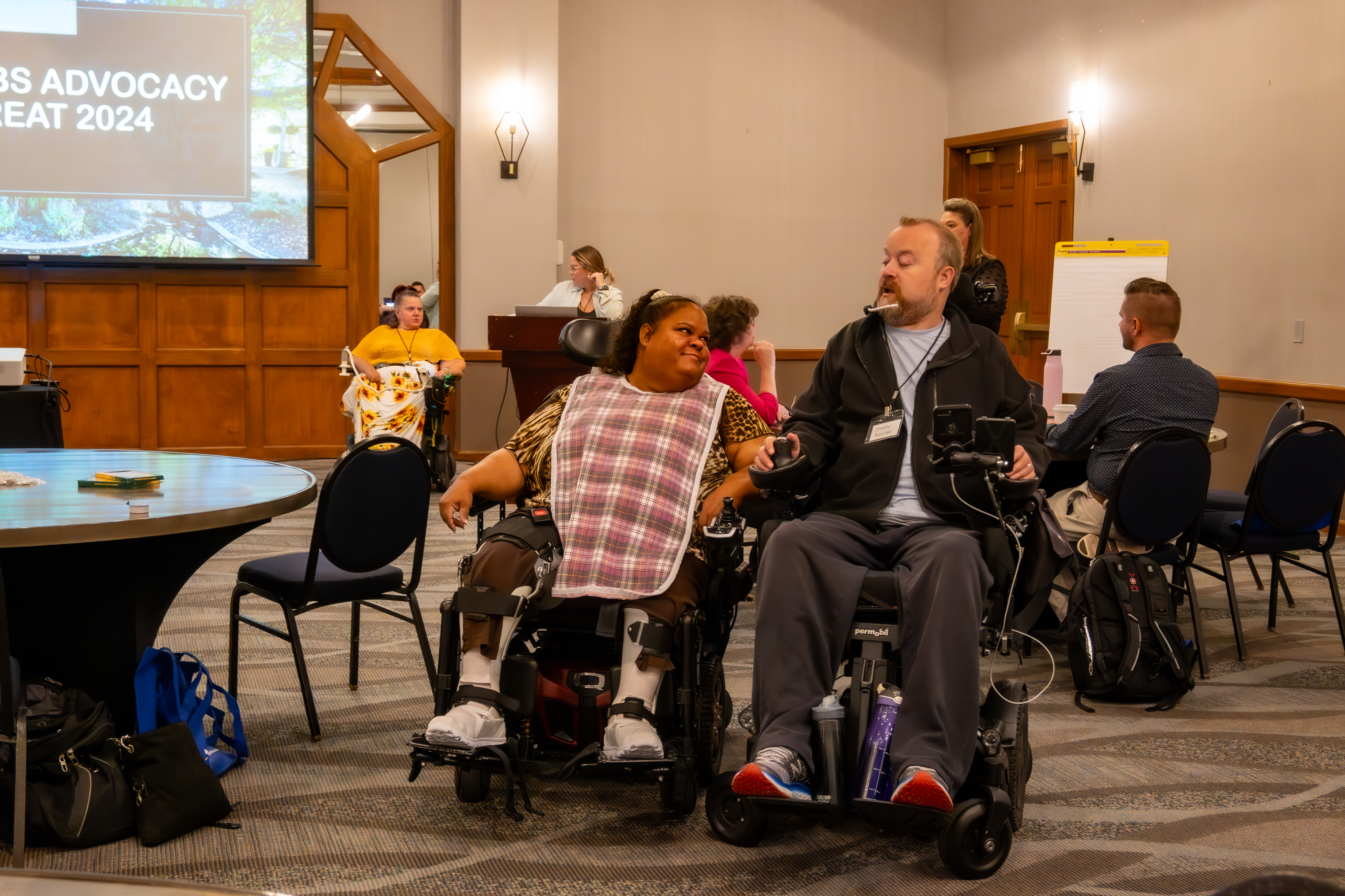 Two OOTF advocates sit side by side in their power chairs and share a laugh